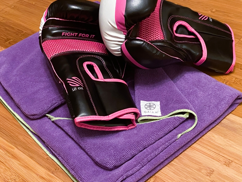 Two pink and black boxing gloves resting on top of a purple Gaiam yoga mat 