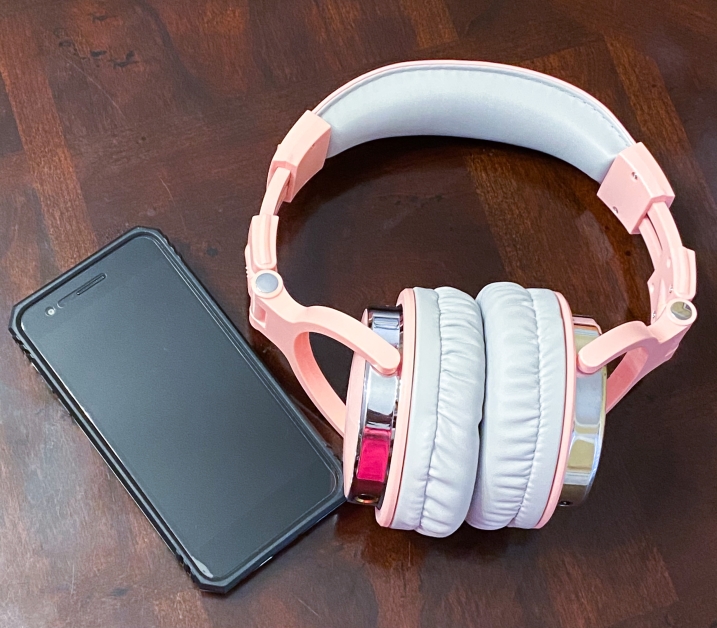 cell phone and pink headphones on a brown, wooden table