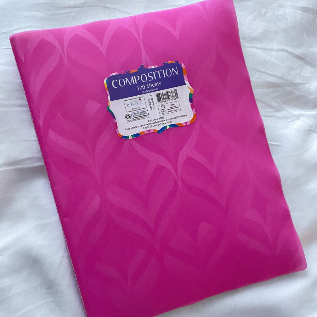 pink composition notebook on top of crisp, white sheets
