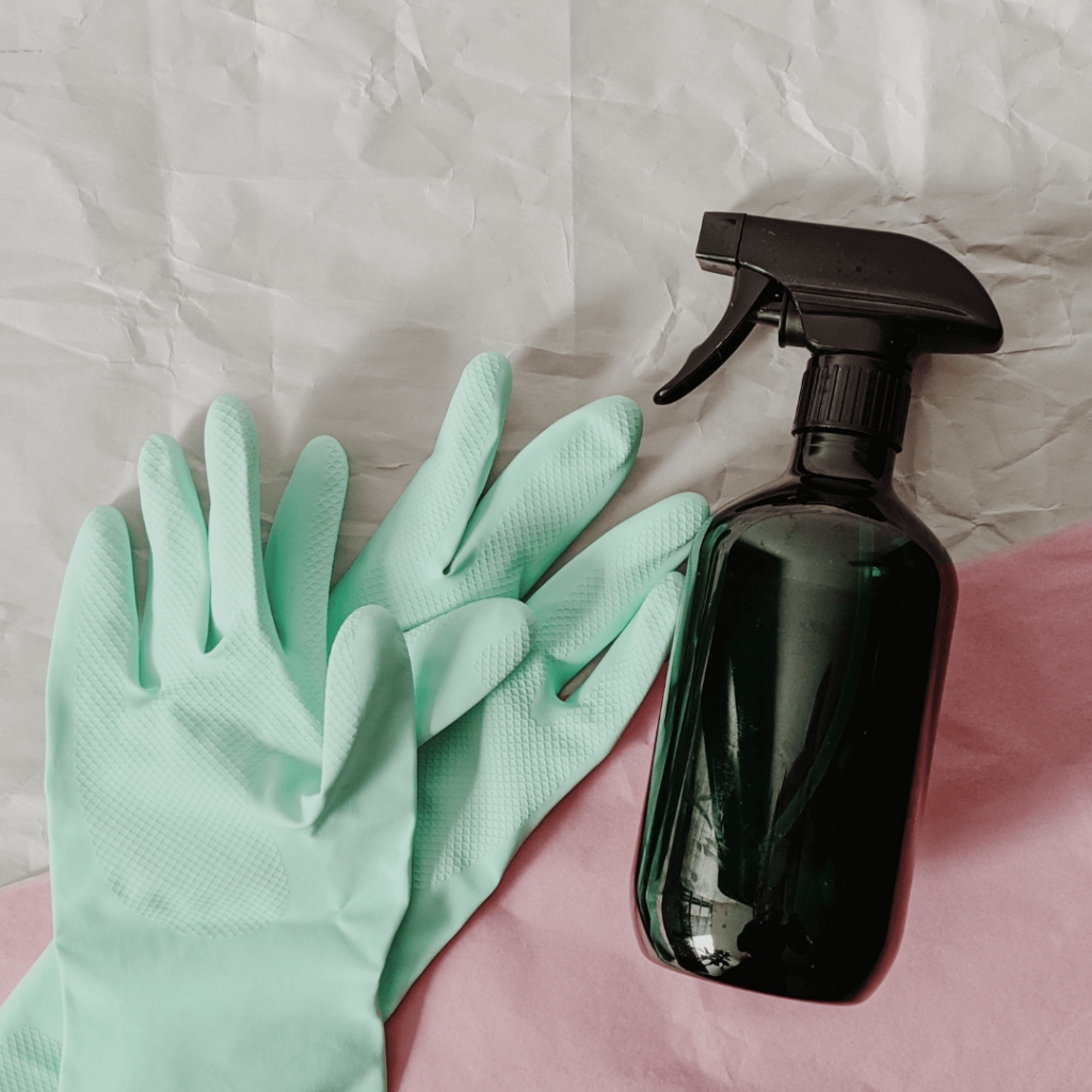 mint green gloves and a glass amber spray bottle on top of a pink towel