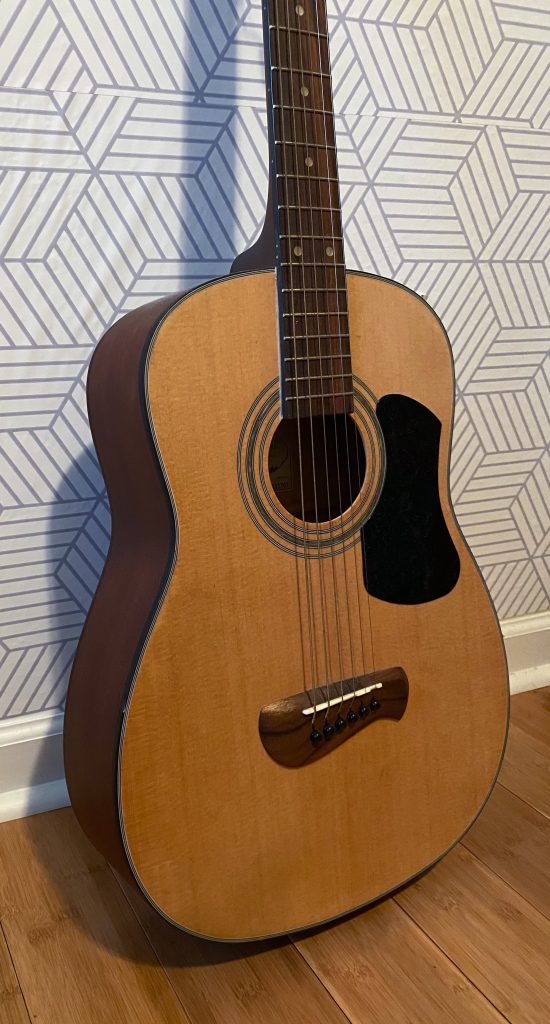 brown acoustic guitar leaning against a neutral-colored wall